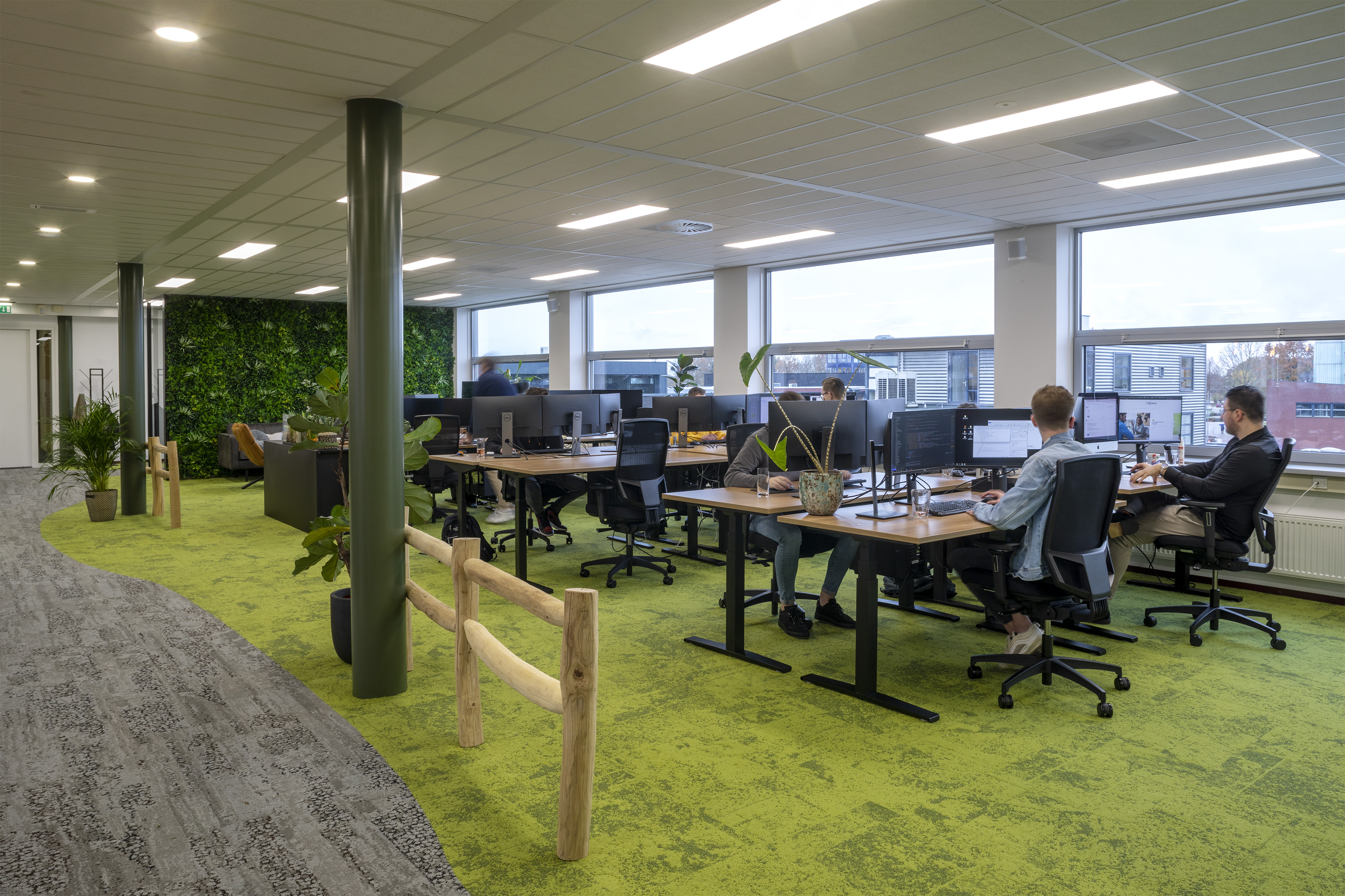 Open kantoorruimte met zit-sta bureaus en ergonomische bureaustoelen op groen tapijt met plantenwand